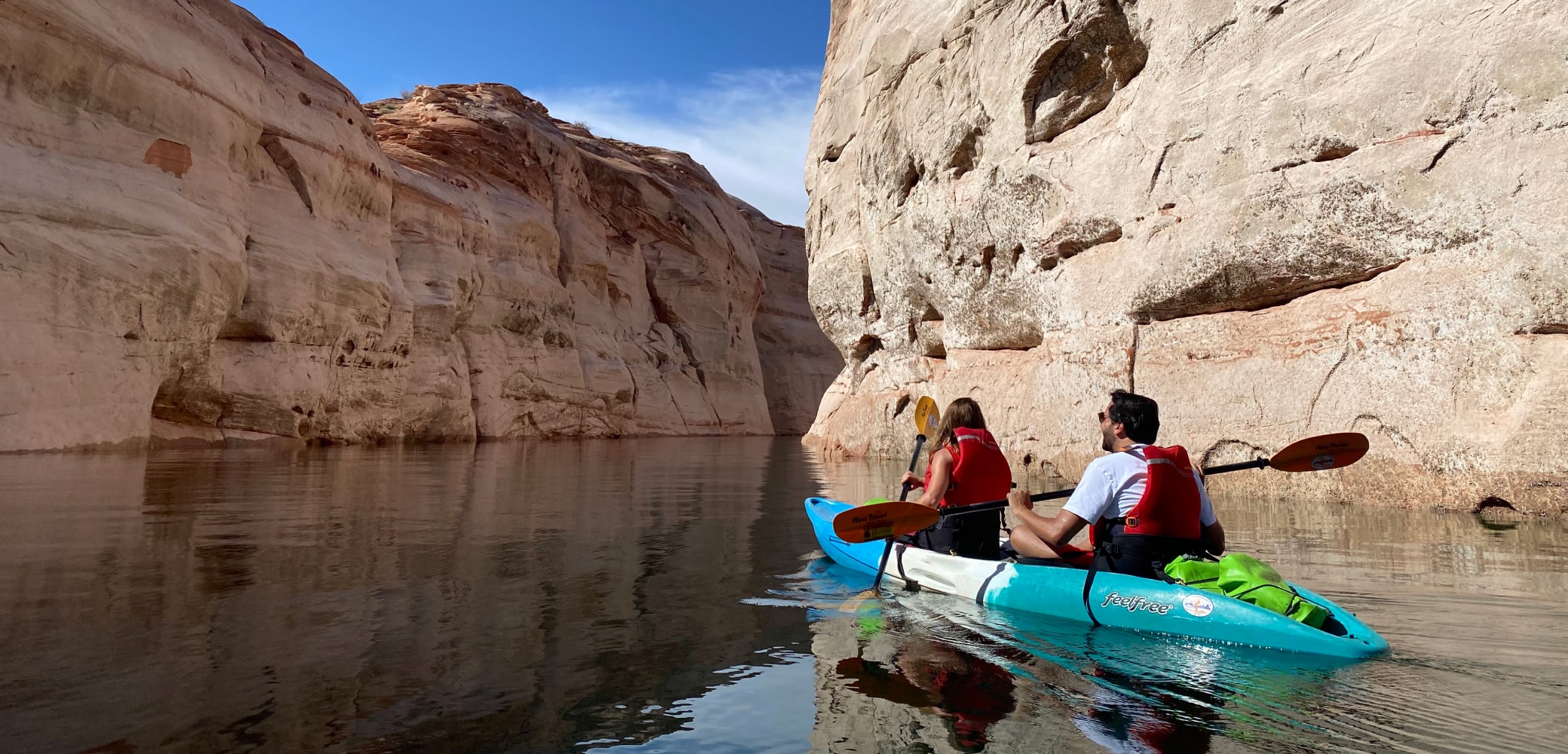 two people in a double kayak paddling through a small canyon of lake powell on a private tour