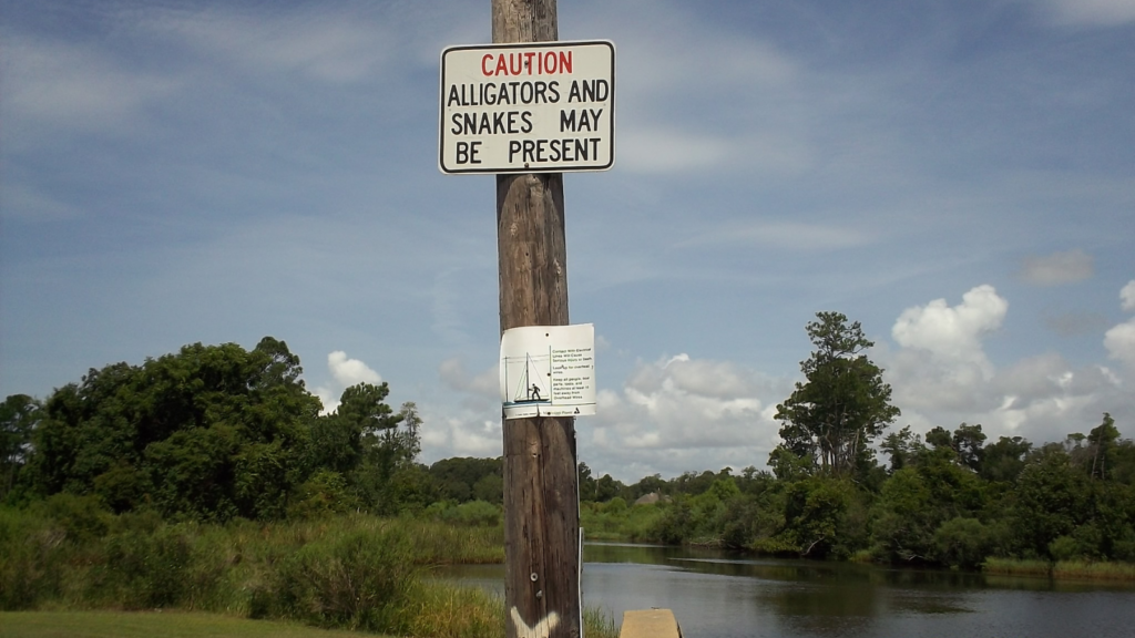 A sign in front of a river warning that alligators and snakes may be present