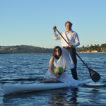a bride and groom stand on a paddleboard
