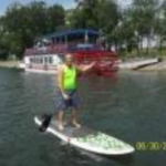 a man in a green shirt stand on a paddleboard in a harbor