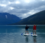a man and woman smile on paddleboards in Alaska