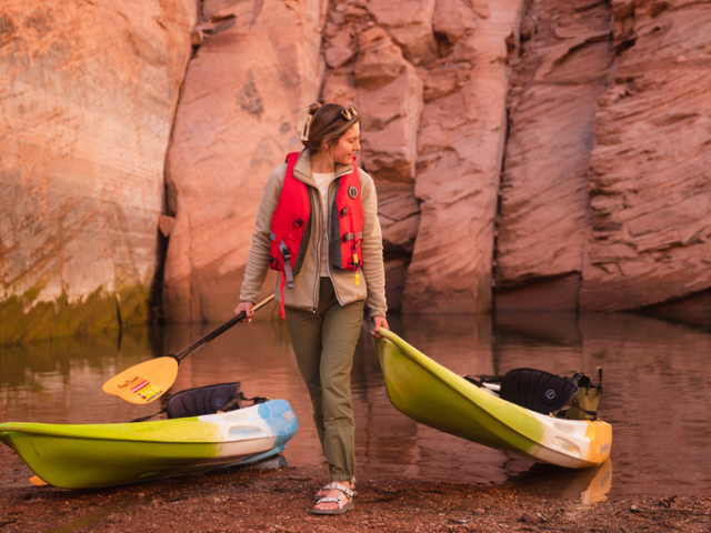 A woman walks a kayak onto shore in a canyon