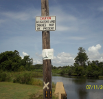 a sign stating alligators may be present hangs in front of a river