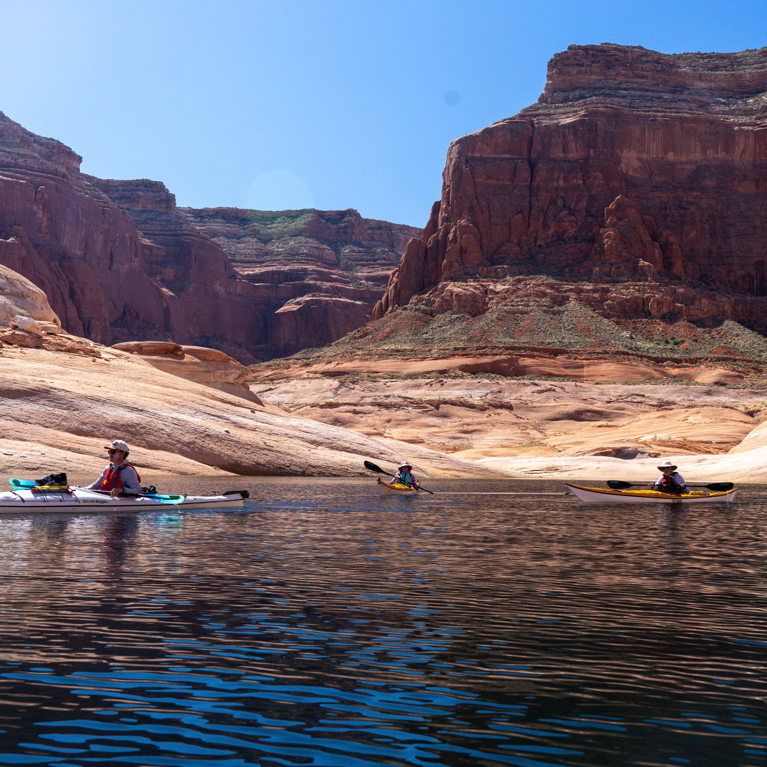 Three paddlers in hats and sun gear in individual kayaks