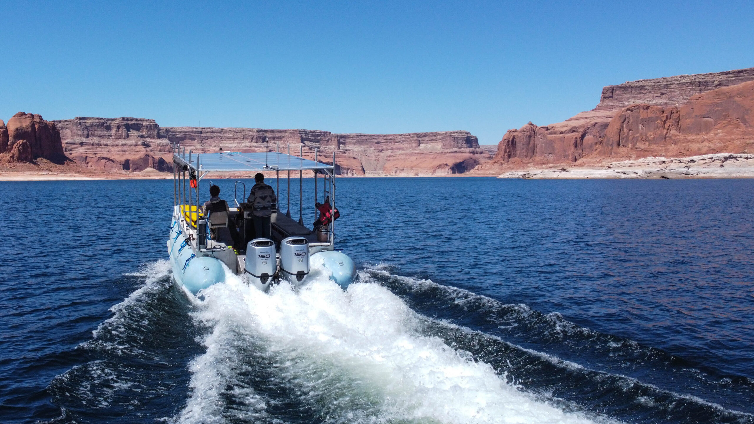 A blue pontoon boat with two motors picks a white wake