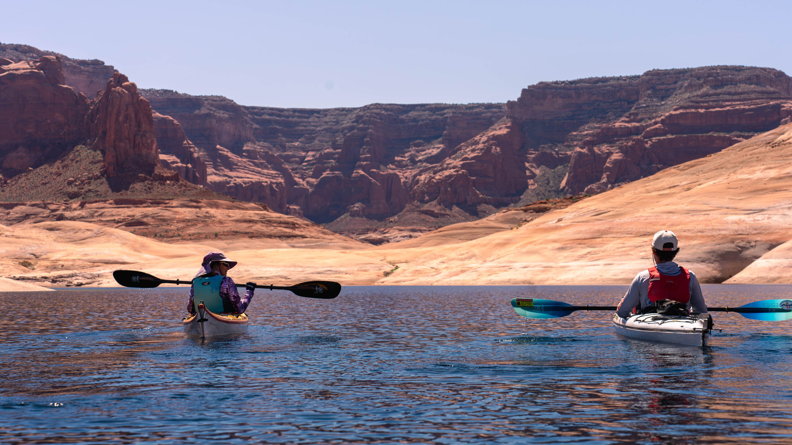 One kayaker looks at another while paddling on Lake Powell on a sunny day